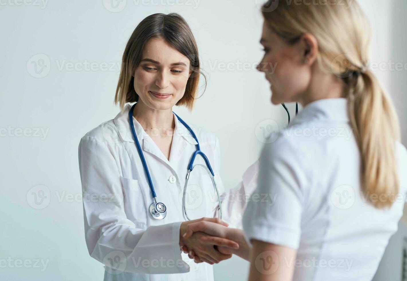 beautiful woman doctor with stethoscope shaking hands with female patient photo