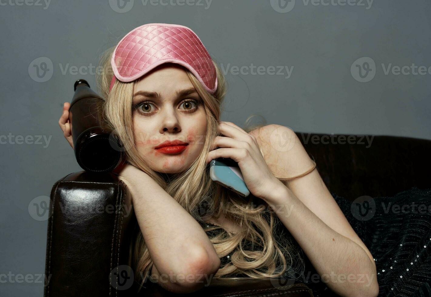 un mujer en un rosado máscara mentiras en el sofá con un botella de cerveza y un teléfono en su mano foto
