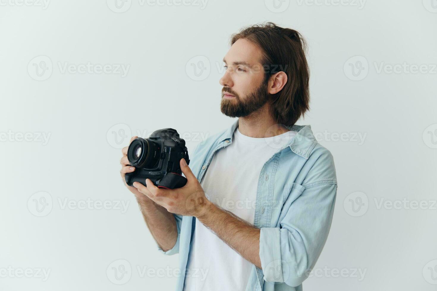 un masculino hipster fotógrafo en un estudio en contra un blanco antecedentes mira mediante el cámara visor y dispara disparos con natural ligero desde el ventana. estilo de vida trabajo como un Lanza libre fotógrafo foto