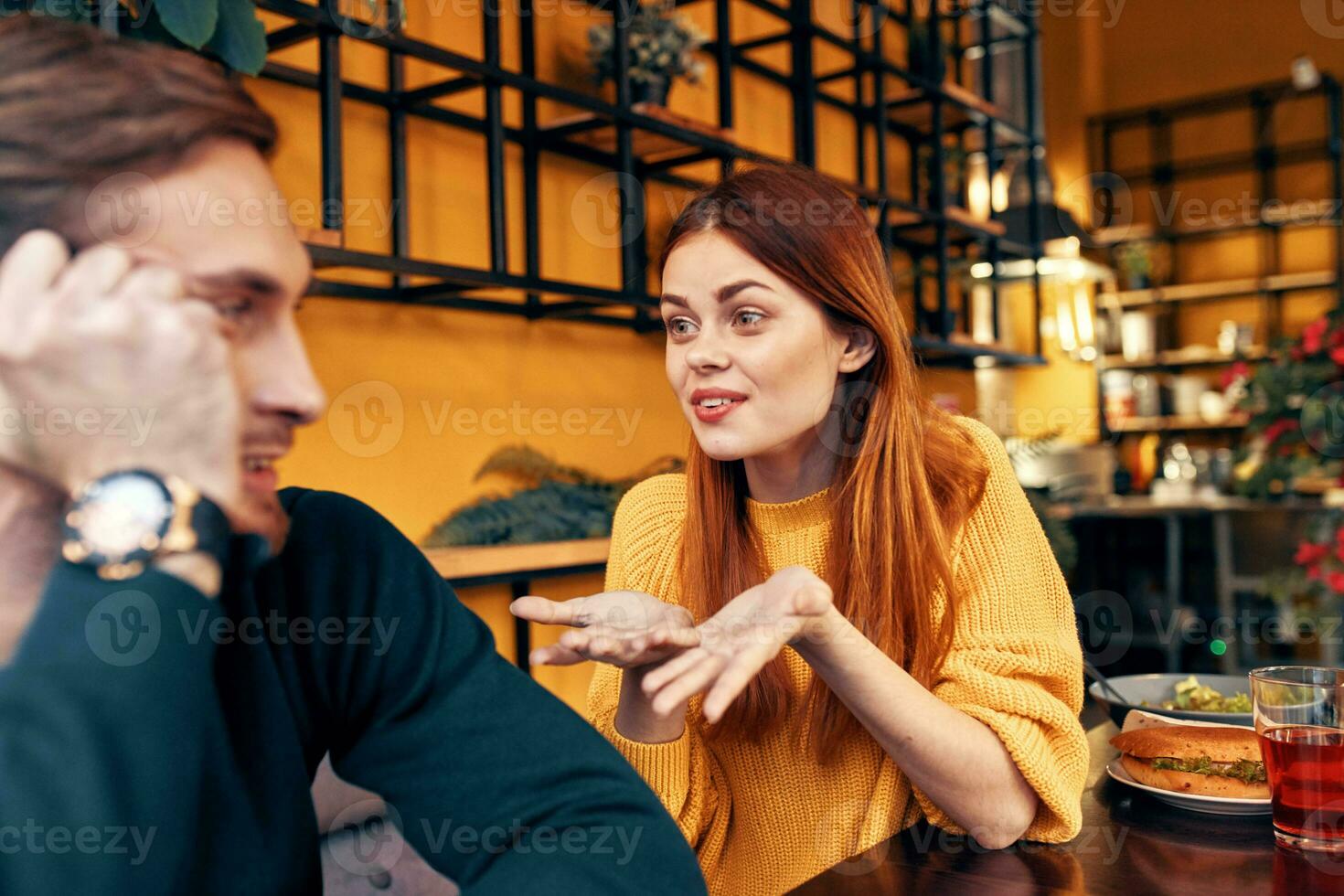 happy woman in a sweater gestures with her hands fun emotions and a man in a sweater sits in a cafe photo