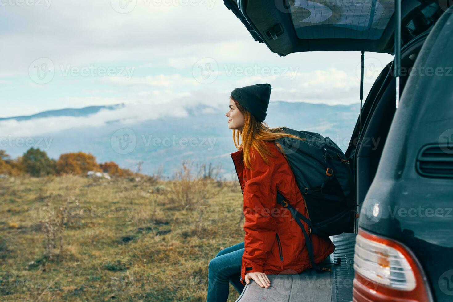 woman tourist with a backpack sits on the trunk of a car in the mountains in autumn in nature photo