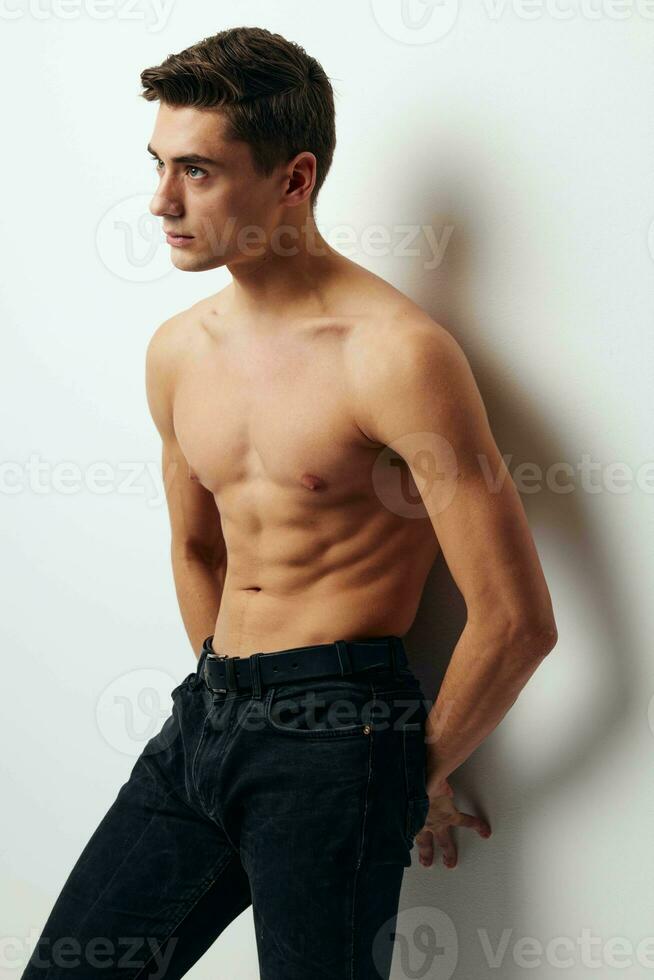Side view of a man in trousers with a bare torso leaning against the wall photo