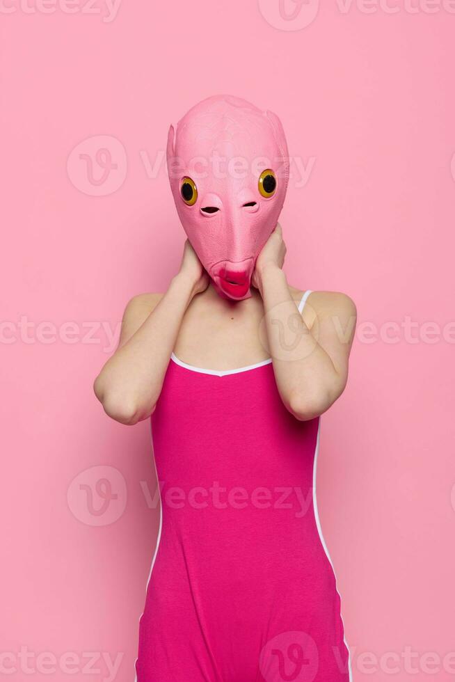 mujer en un pescado disfraz para Víspera de Todos los Santos poses en contra un rosado antecedentes en un loco de miedo disfraz con un rosado silicona máscara en su cabeza foto