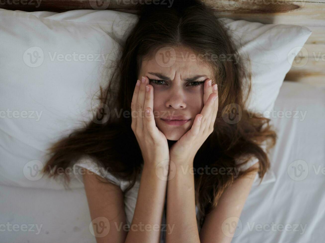 upset woman holding face with hands while lying in bed health problems photo