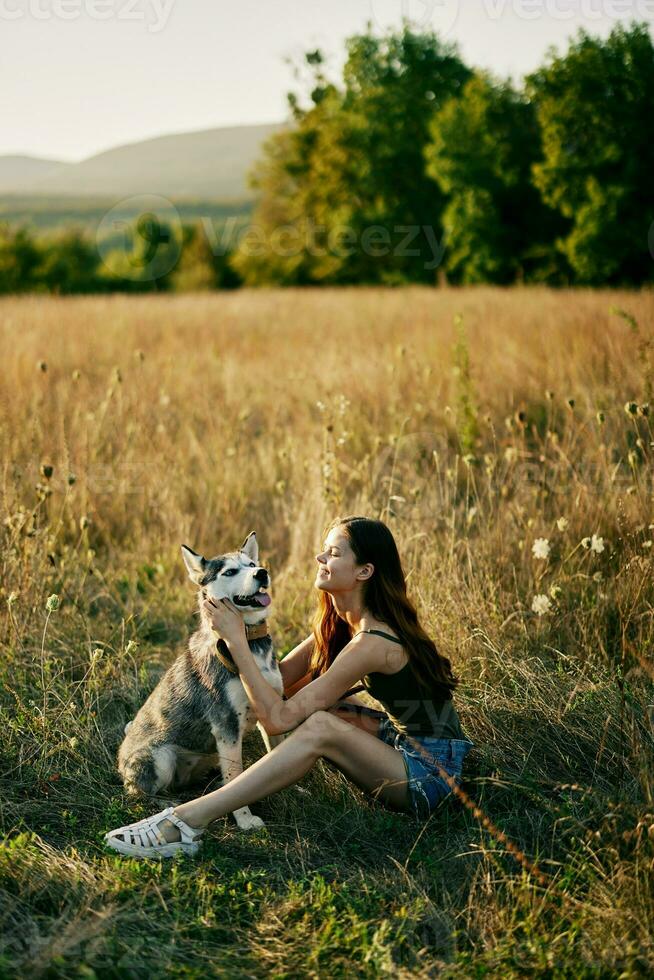 Woman sitting in field with dachshund dog smiling while spending time in nature with friend dog in autumn at sunset while traveling photo