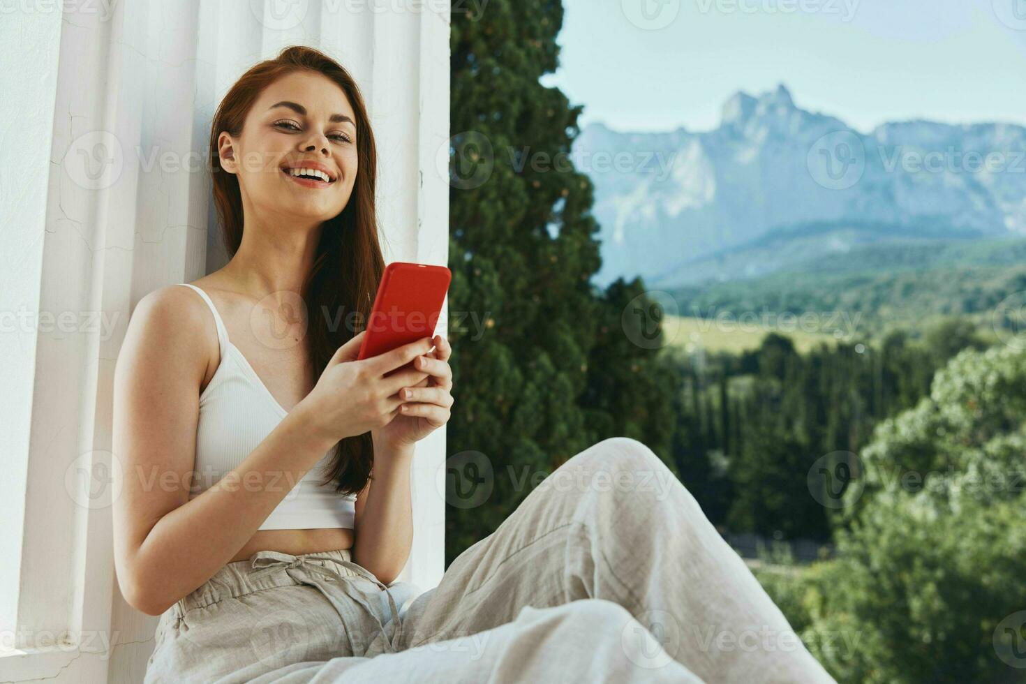 alegre mujer sentado en el balcón con teléfono hermosa montaña ver verano relajación concepto foto