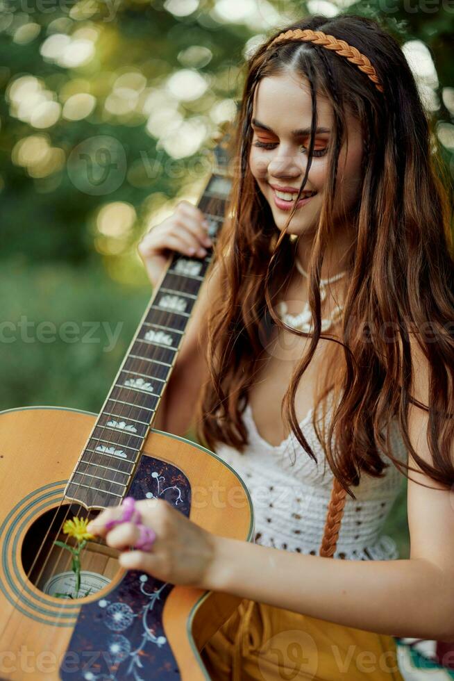 Happy hippie woman with a guitar relaxing in nature sitting on a plaid smiling and enjoying the view. Lifestyle in harmony with nature and self photo