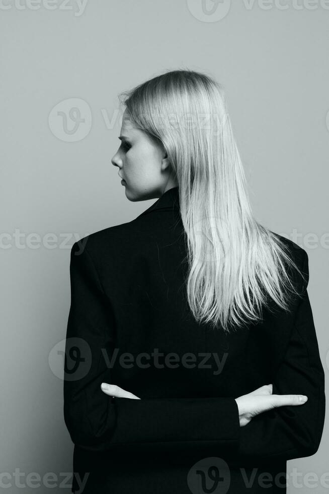 The concept of art photography. A stylish girl crosses her arms behind her back turns her head and poses with her back in a black jacket in the studio. Fashion banner photo