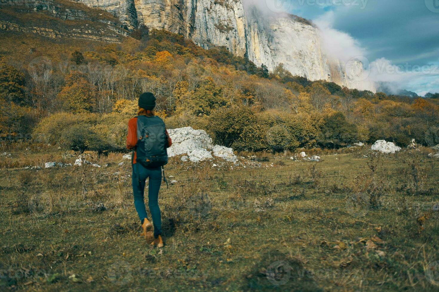 woman in jeans boots and a sweater with a backpack are resting in the autumn in the mountains in nature photo