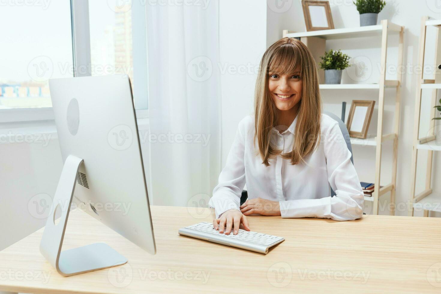 Smiling cheerful adorable blonde businesswoman worker freelancer look at camera typing project report in light modern office. Happy employee work on computer online in support service. Copy space photo
