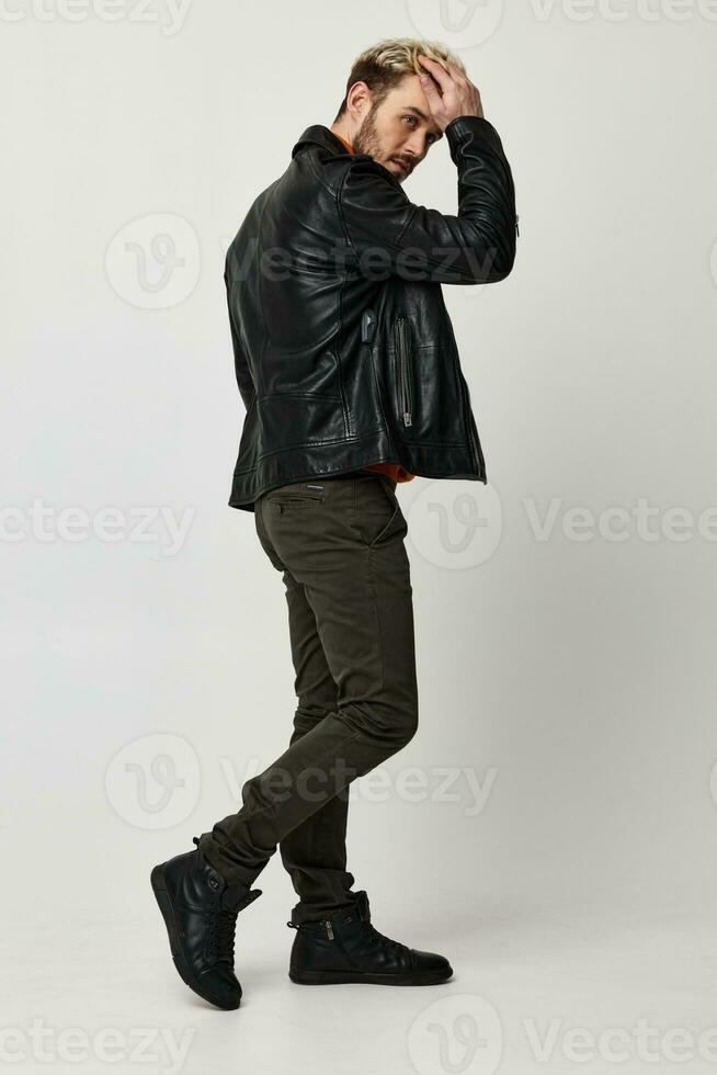 elegant man in a leather jacket touches his head with his hand on a light background and pants model photo