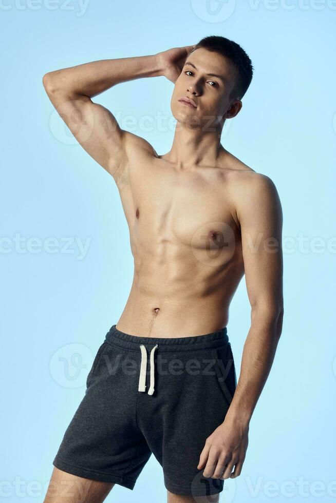 man with pumped up abs holds hand on head posing cropped view blue background photo