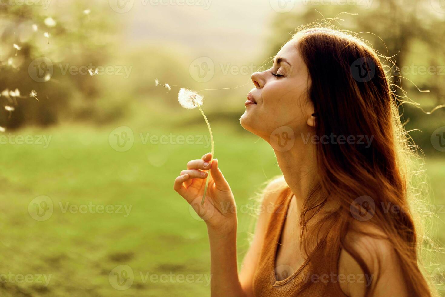 A young woman holds a dandelion in her hands and blows on it, the seeds of the dandelion fly through the air to grow new flowers. Caring for the Earth's Ecology photo