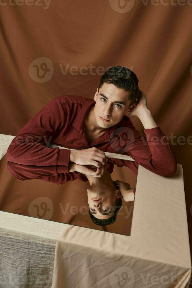 a man on a fabric background bent to the side and sits at a table with a mirror photo