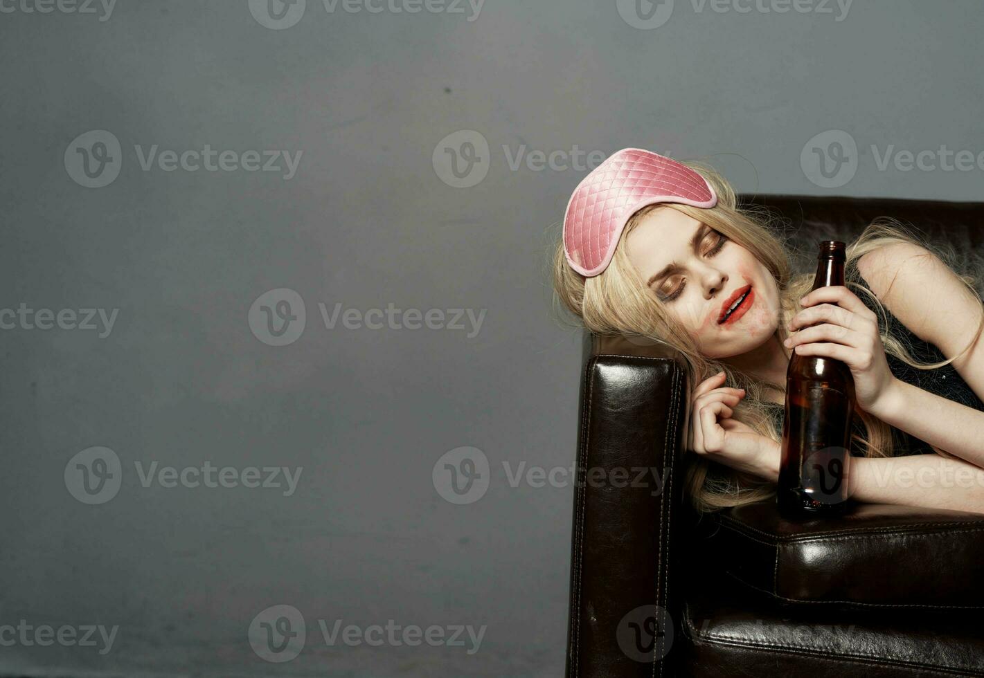 A woman with a pink mask on her head and a bottle of beer sleeps on the couch photo