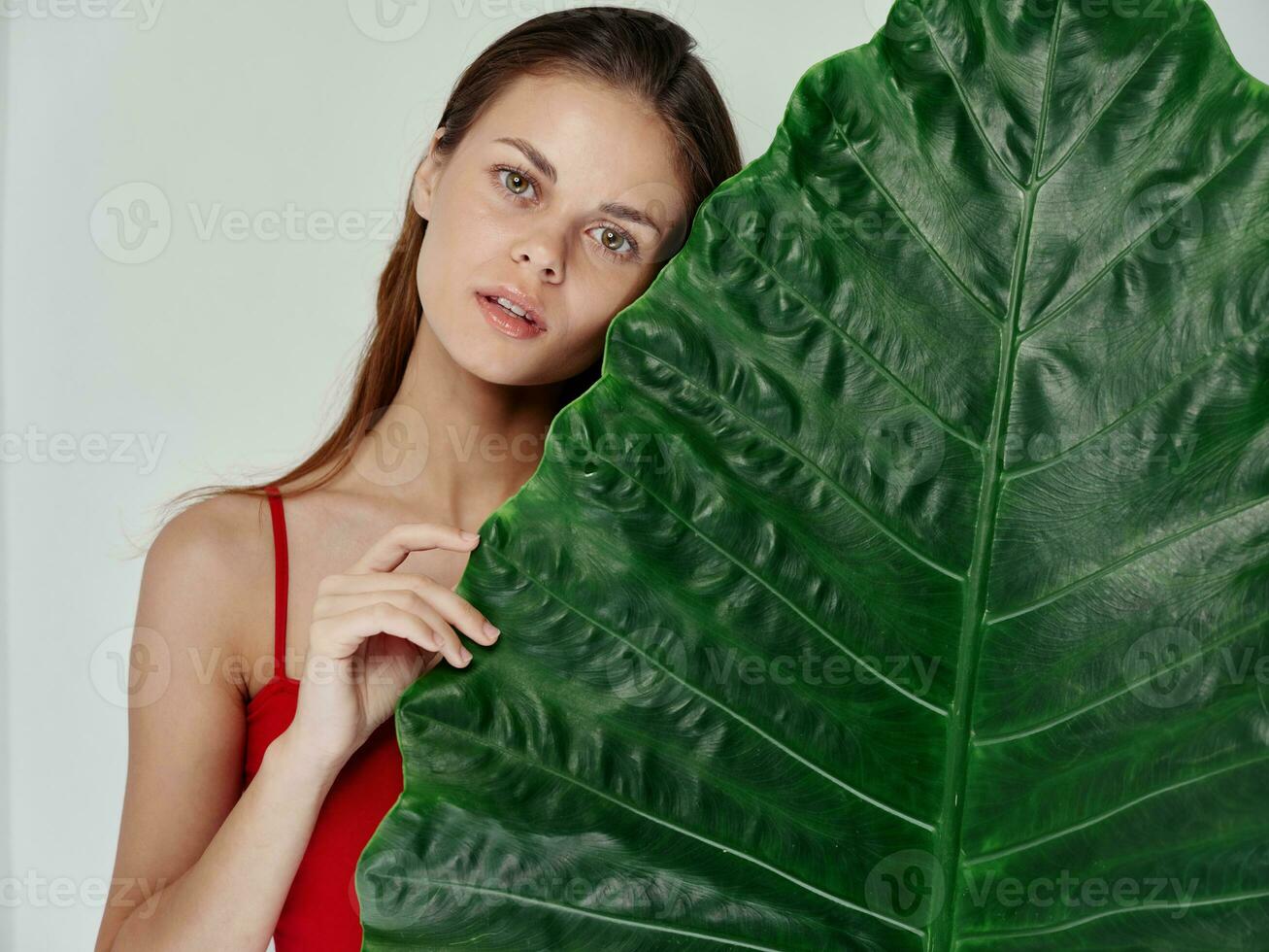 woman in a red t-shirt stands behind a green leaf of a palm tree on a light background photo