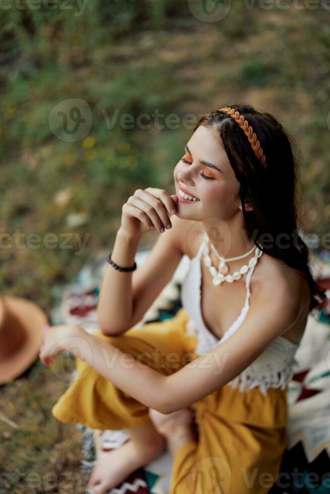 Young beautiful hippie woman sitting on the ground in nature in the fall in eco clothing in the sunset light, a lifestyle of travel and harmony with the world photo