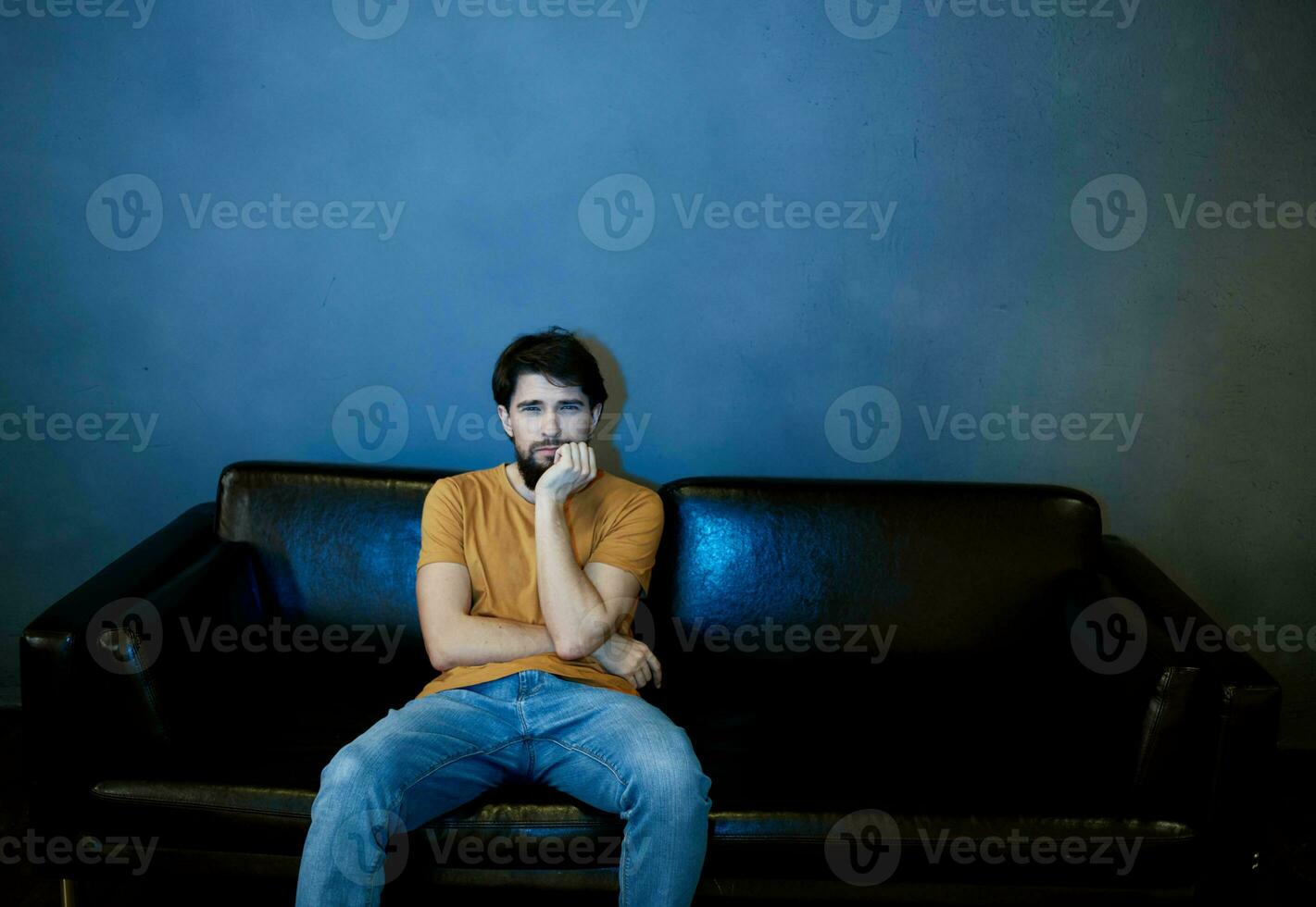 A man sits on a sofa indoors and watches TV front view photo