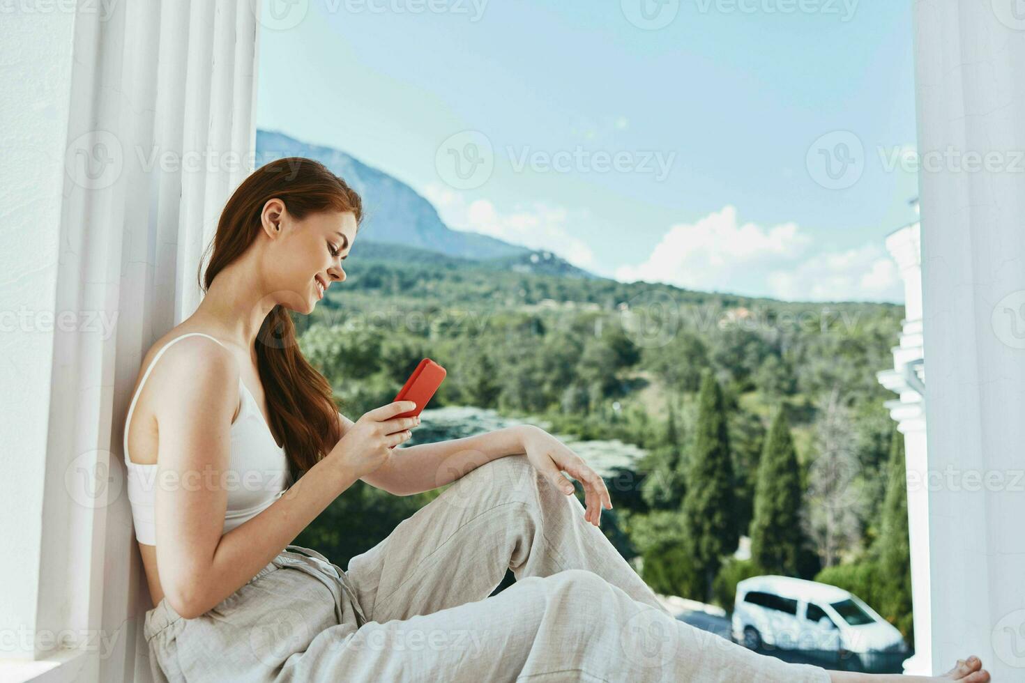 atractivo joven mujer utilizar el teléfono mira a el pantalla en un cómodo hotel un abierto ver de el relajación concepto foto