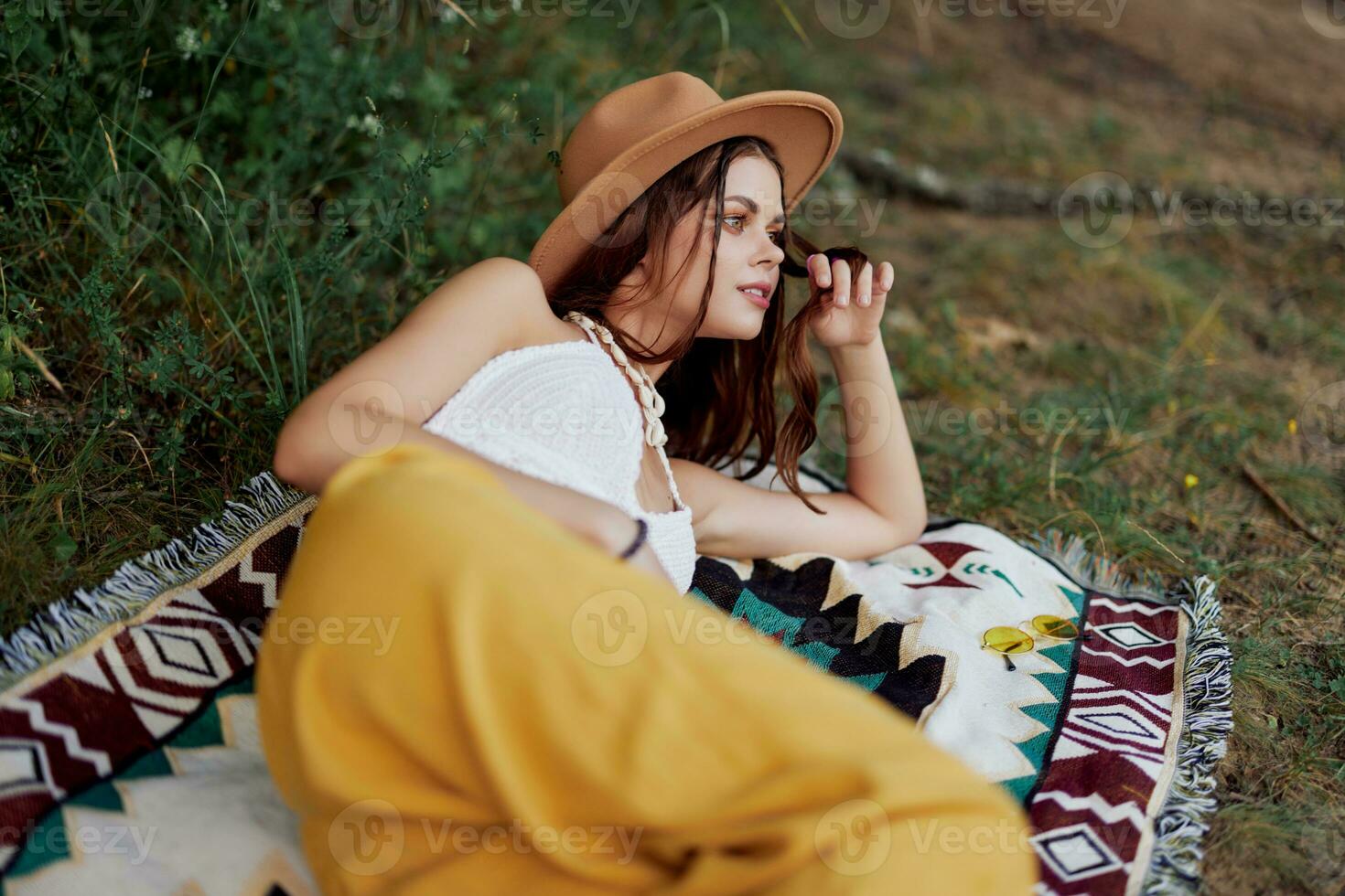 un mujer en Respetuoso del medio ambiente ropa en un hippie Mira es acostado en un de colores tartán sonriente y mirando a un otoño puesta de sol en naturaleza en el parque. estilo de vida en un viaje de armonía con el mundo foto