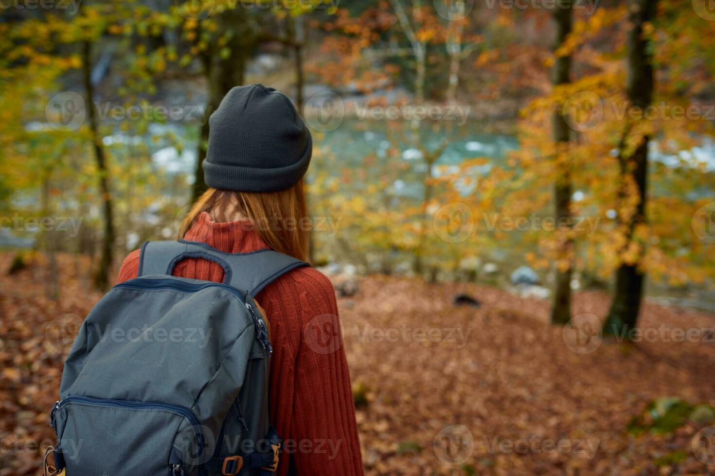woman in a sweater with a backpack on her back near the river in the mountains and park trees autumn landscape photo