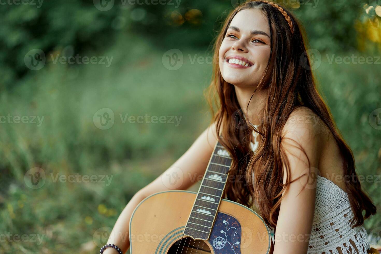 hippie mujer sonriente y abrazando su guitarra en naturaleza en el parque en el puesta de sol ligero foto