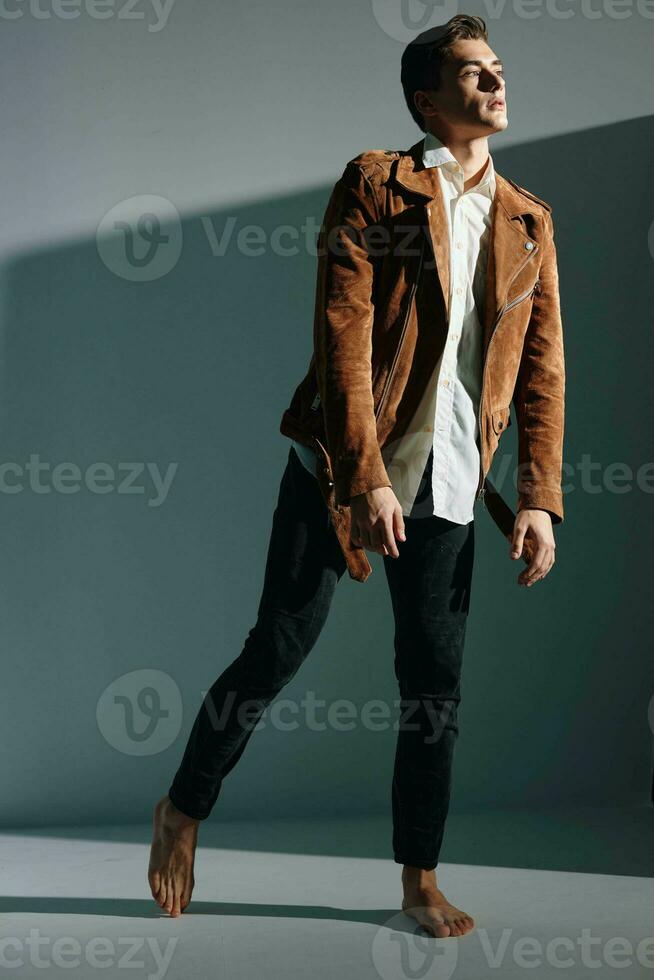 A man in jeans and a brown jacket looking to the side on a gray background bottom view photo