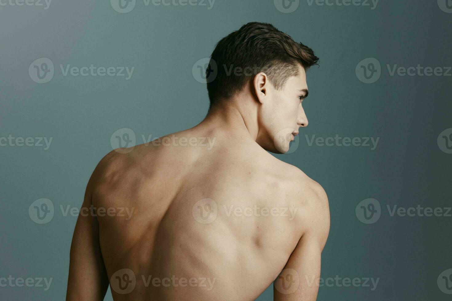 Sexy man with a naked back looks to the side on a gray background rear view of a fitness photo