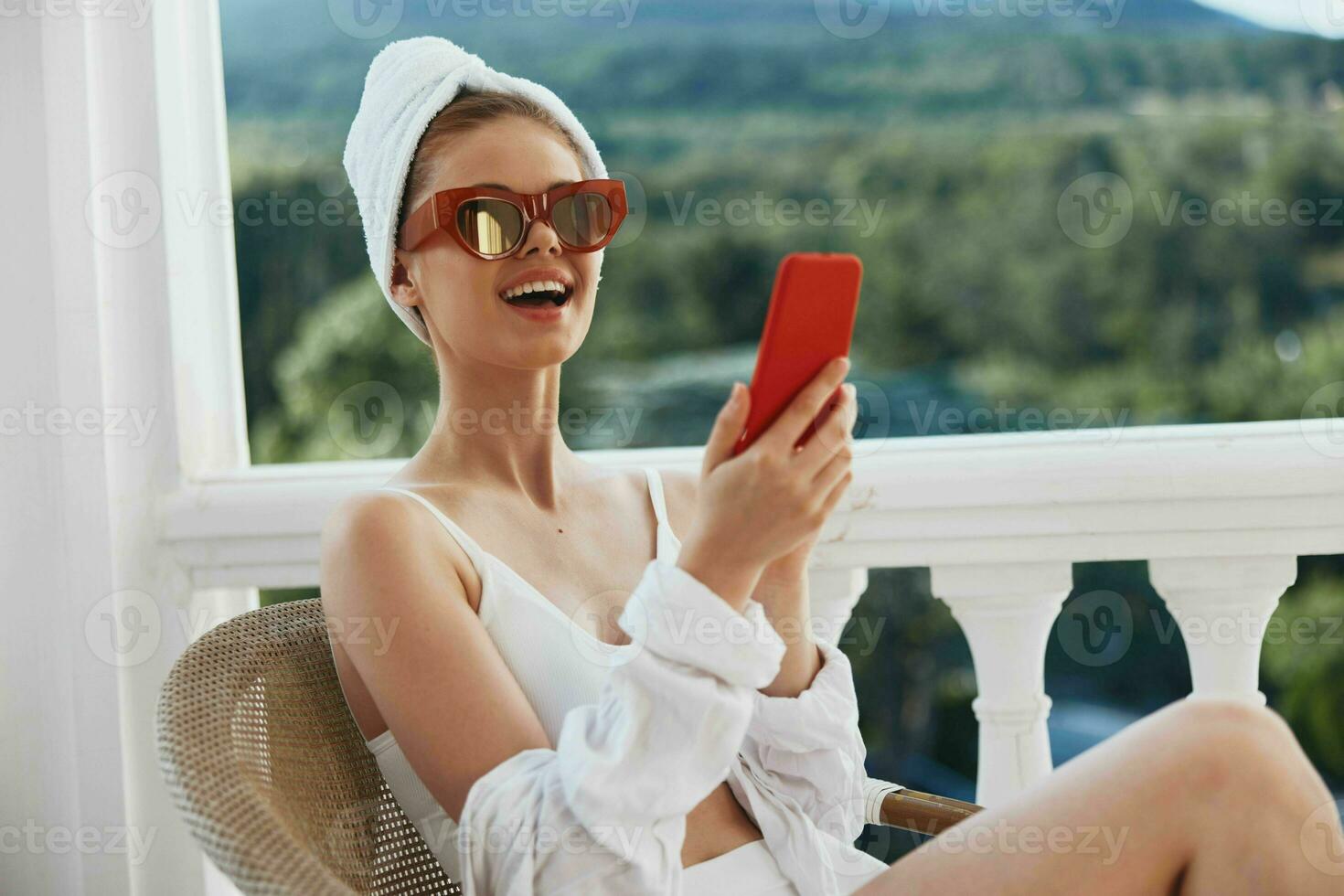 retrato de joven mujer disfrutando el Mañana en el balcón mirando a el móvil teléfono pantalla perezoso Mañana foto