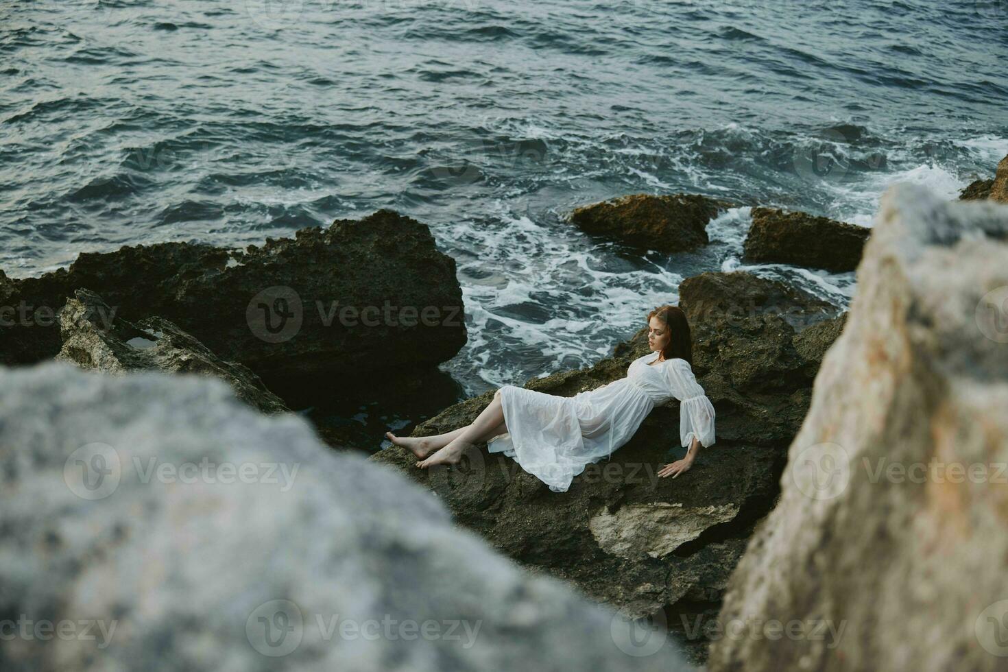 Barefoot woman lying on rocky coast with cracks on rocky surface view from above photo