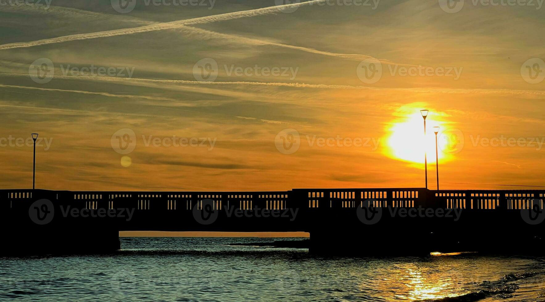 Sunset over the sea with jetty in silhouette photo