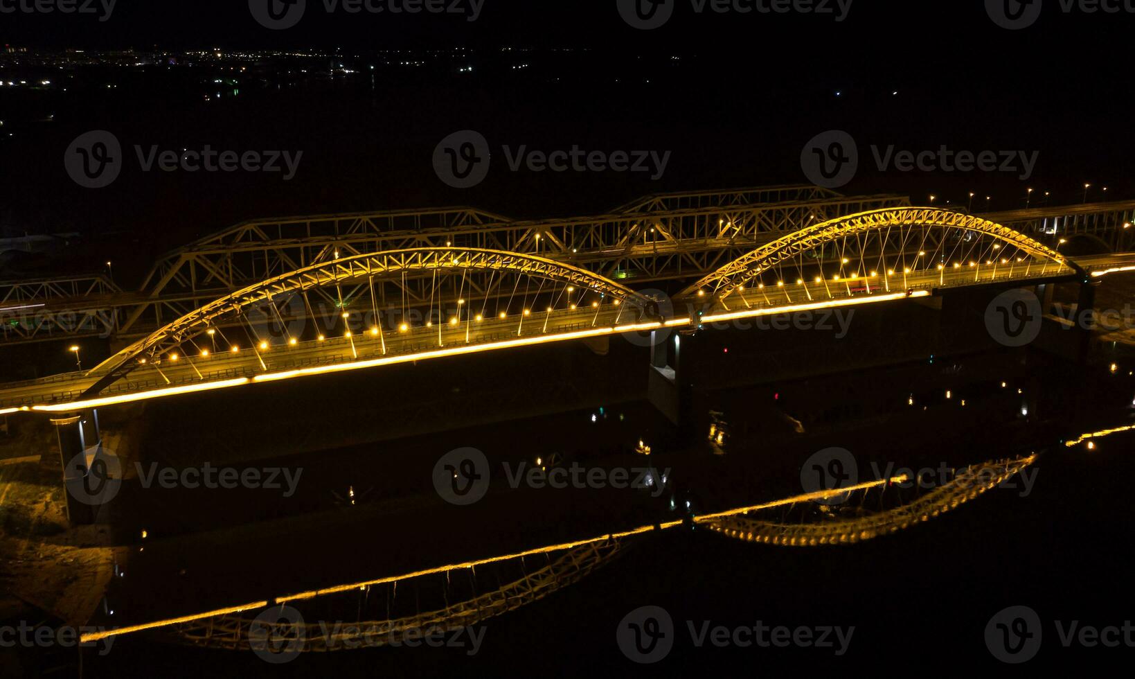 Bright lights, bridges with arches, night city. A road bridge across the river, taken from a drone. photo