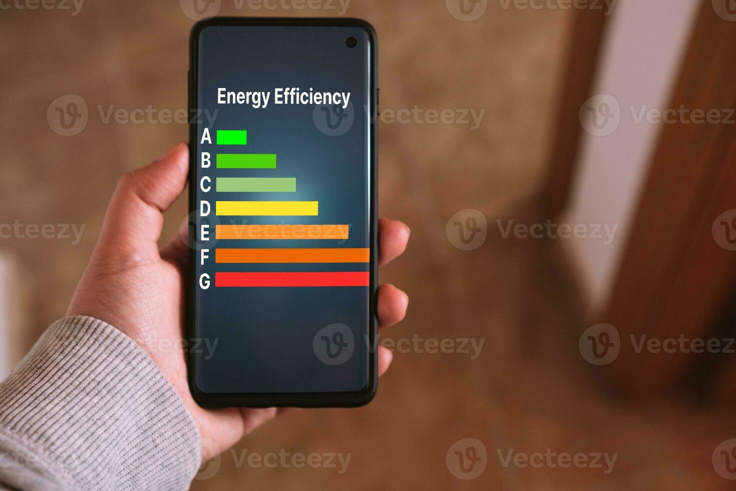Woman's hand holds a smartphone with a Energy efficiency rating labels on screen. Low consumption and efficient products. Reduce carbon footprint. Green eco-friendly business. Low CO2 emissions. photo
