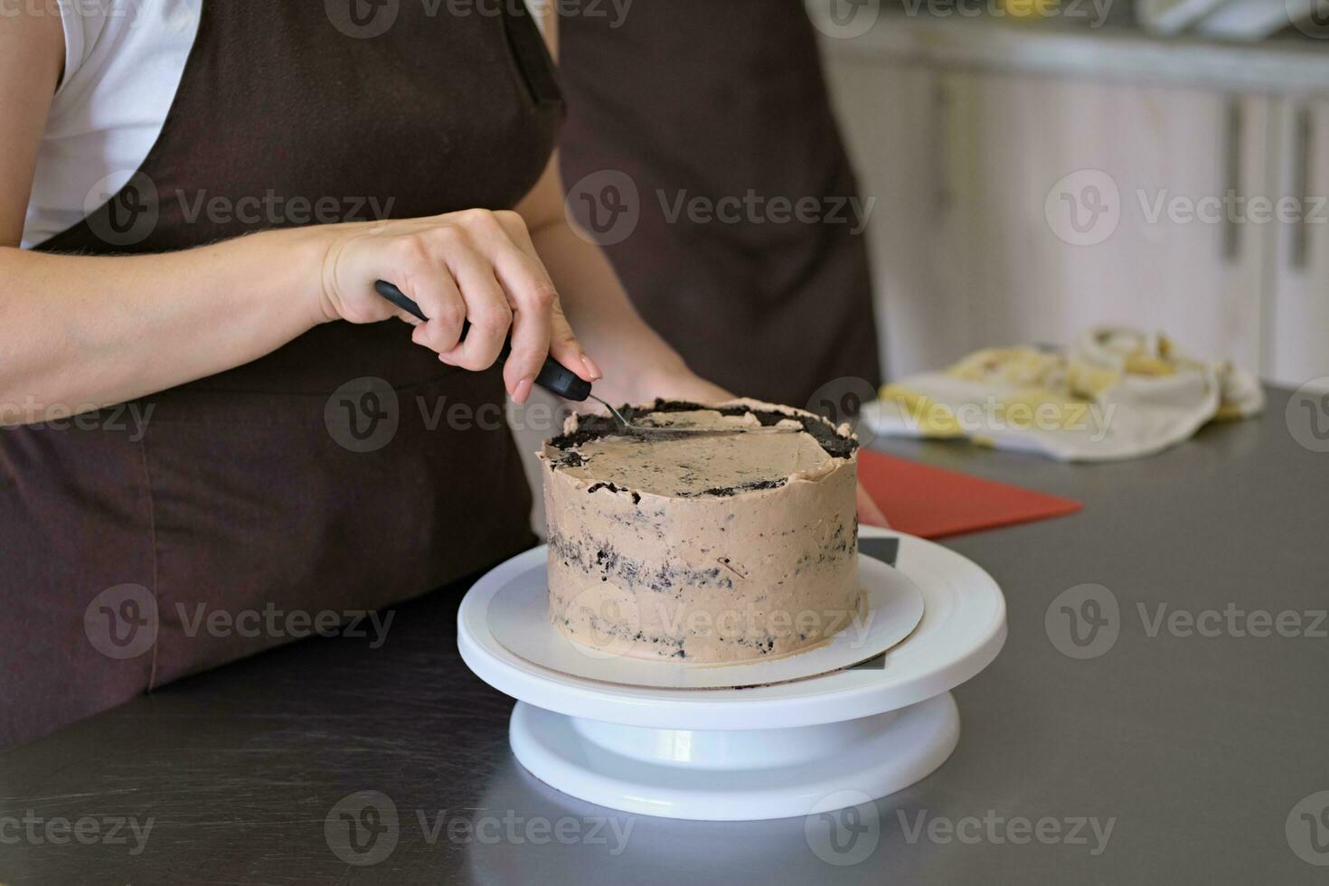 Woman pastry chef lines chocolate cream on chocolate cake, close-up. Cake making process, Selective focus photo