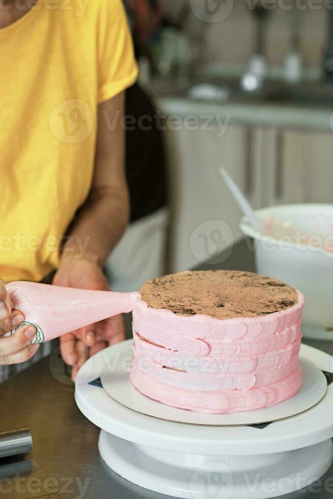 Woman spreads pink cream on cake with pastry bag, close-up. Cake making process, Selective focus photo