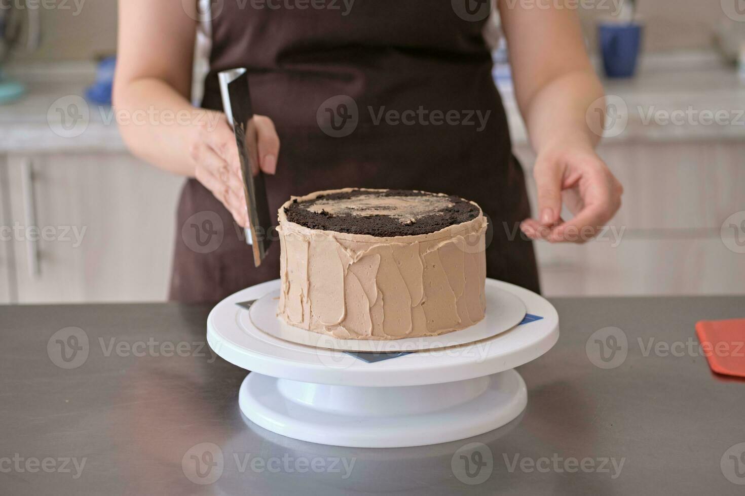 Woman pastry chef lines chocolate cream on chocolate cake, close-up. Cake making process, Selective focus photo