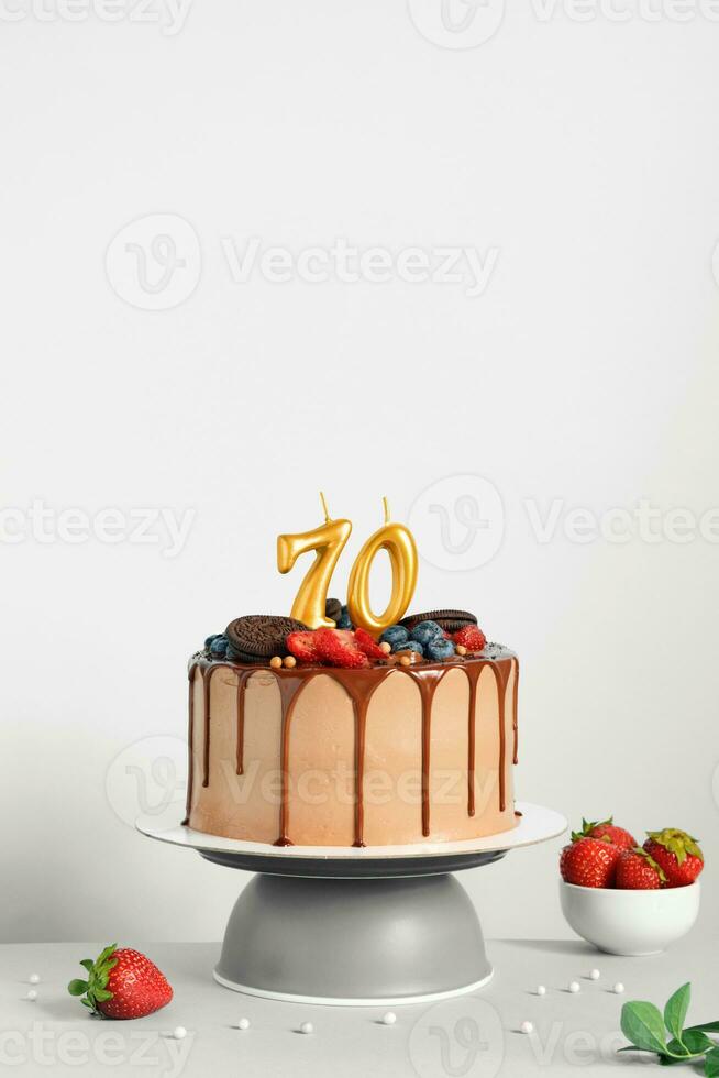 Chocolate birthday cake with berries, cookies and number seventy golden candles on White background, copy space photo