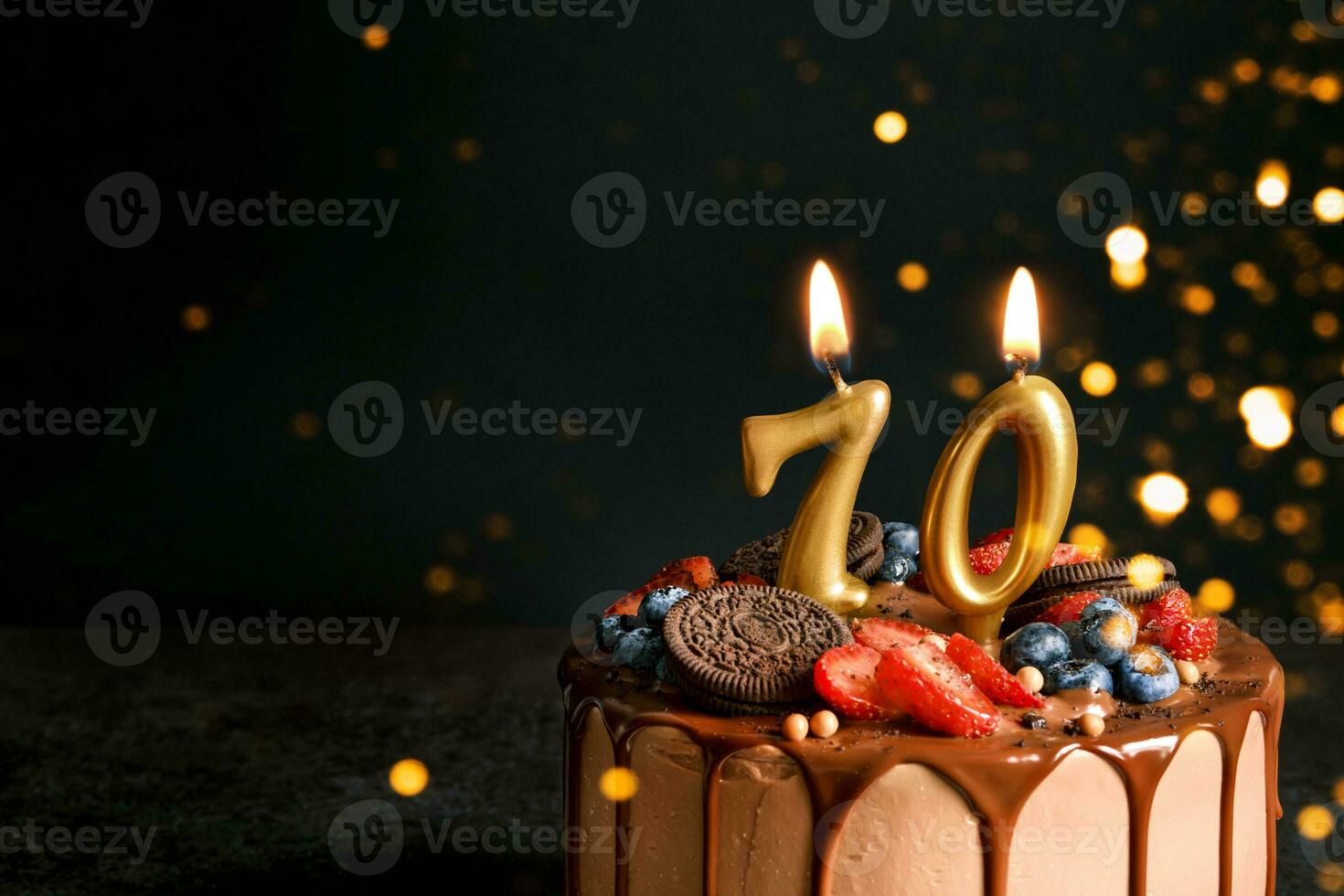 Chocolate birthday cake with berries, cookies and number seventy golden candles on black background, copy space photo