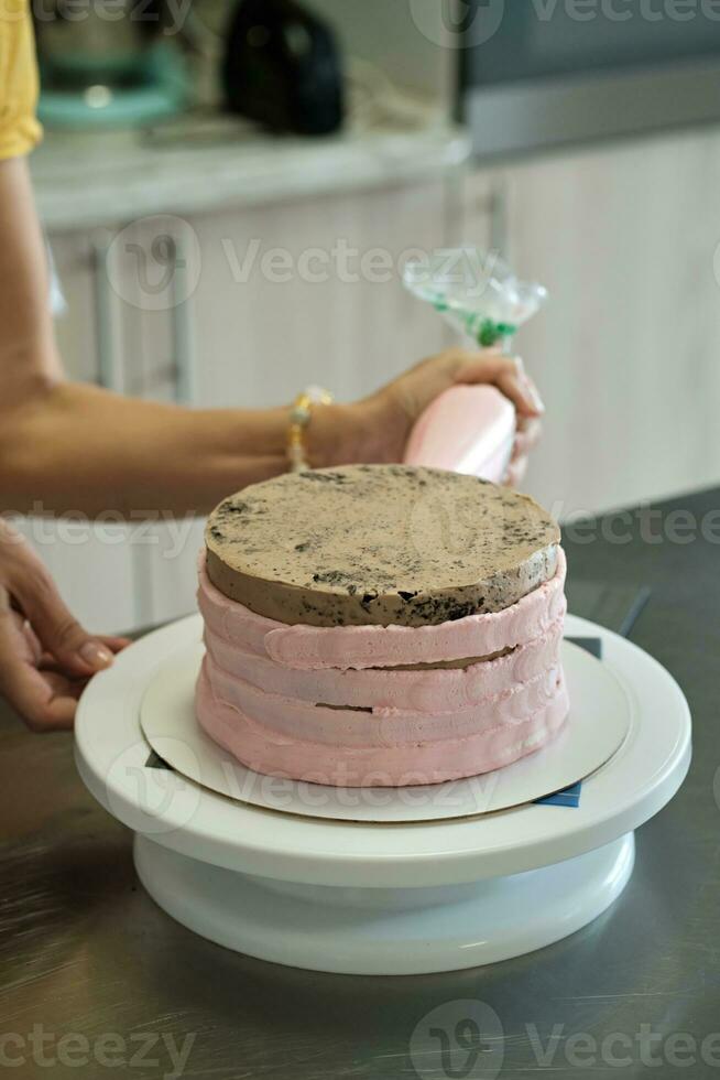 Woman spreads pink cream on cake with pastry bag, close-up. Cake making process, Selective focus photo