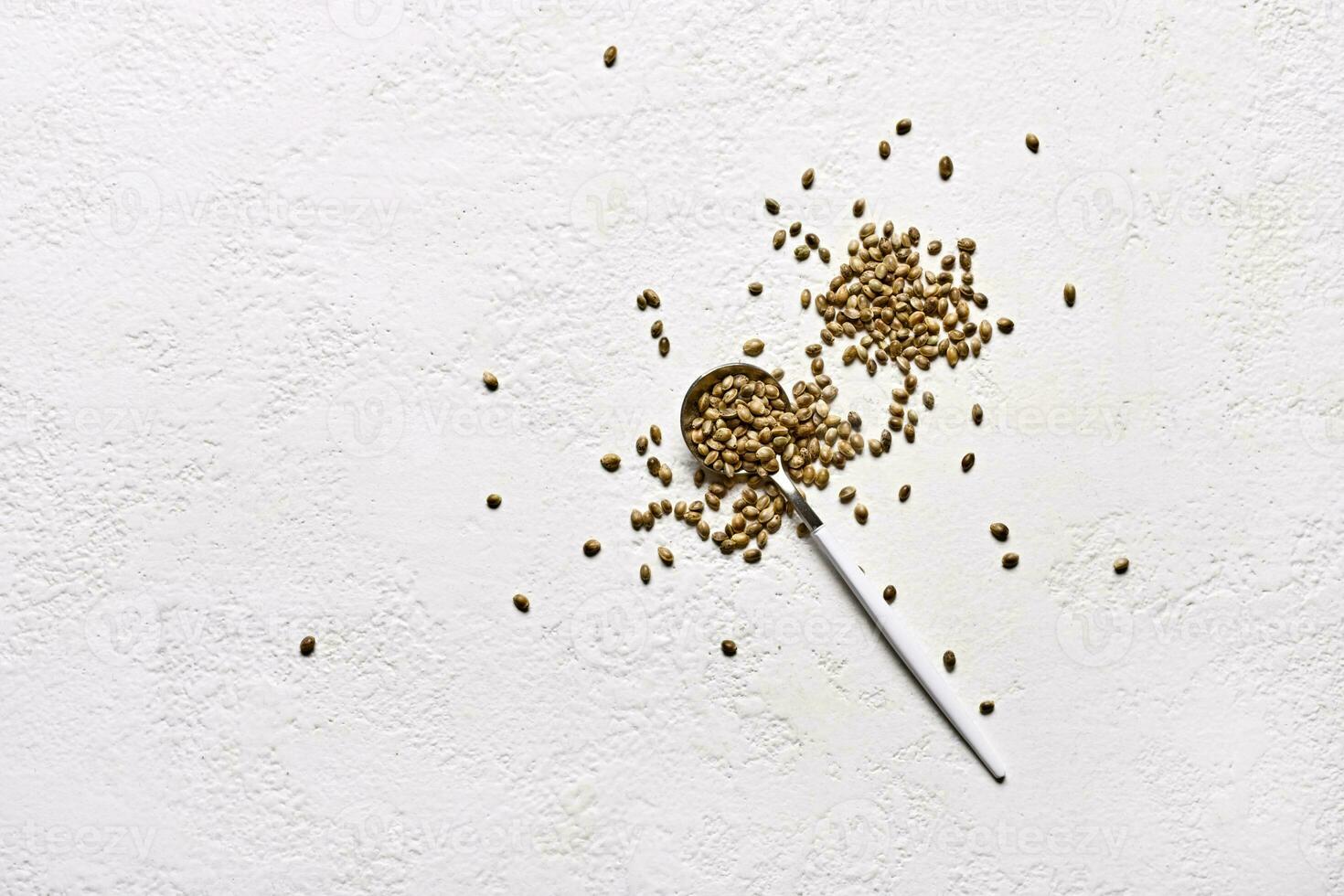 Cannabis seeds in spoon and sprinkled on white background. Top view with copy space photo
