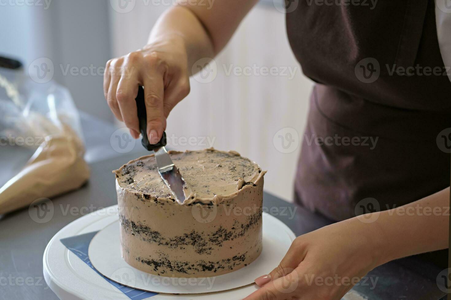 Woman pastry chef lines chocolate cream on chocolate cake, close-up. Cake making process, Selective focus photo