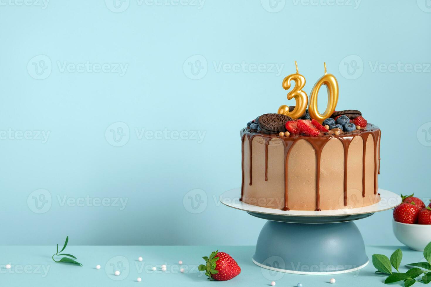 Chocolate birthday cake with berries, cookies and number 30 golden candles on blue wall background, copy space photo
