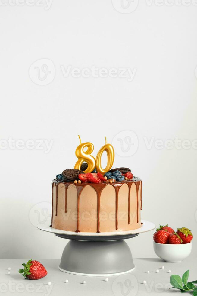 Chocolate birthday cake with berries, cookies and number eighty golden candles on White background, copy space photo