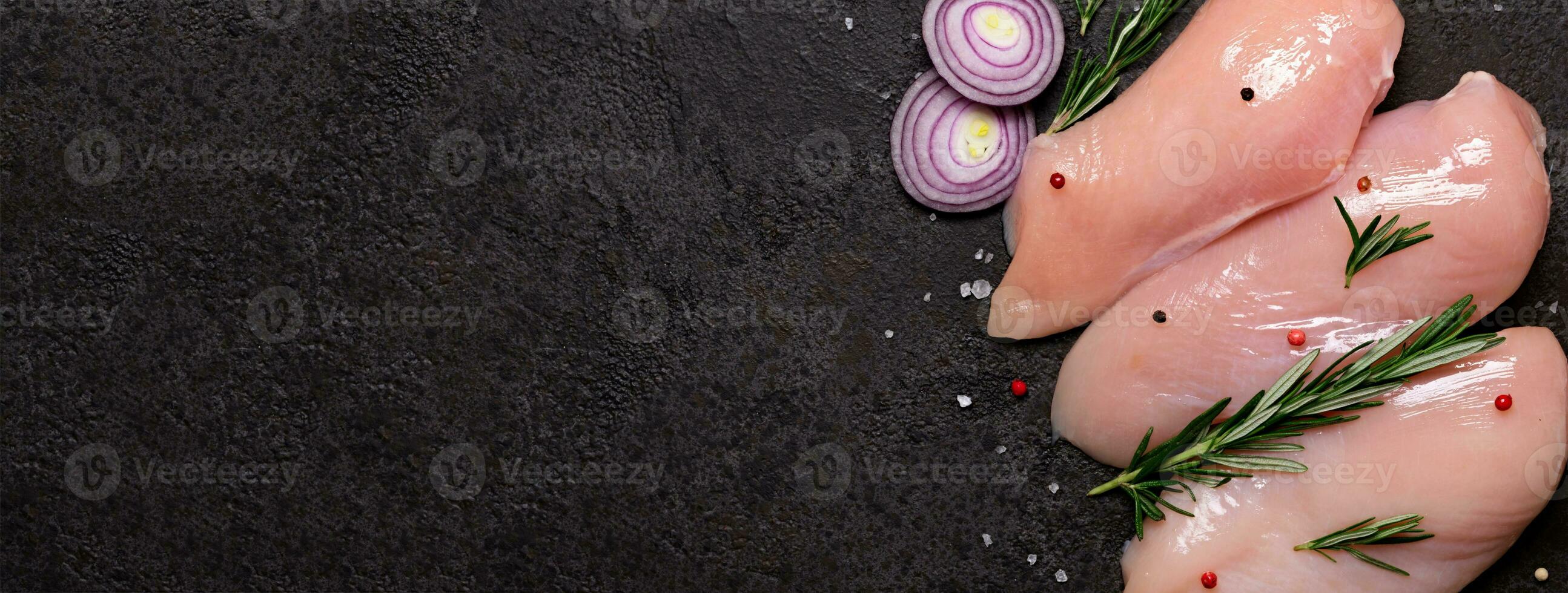 Raw chicken breast with spices and herbs on black stone background. Preparation for cooking, banner format photo