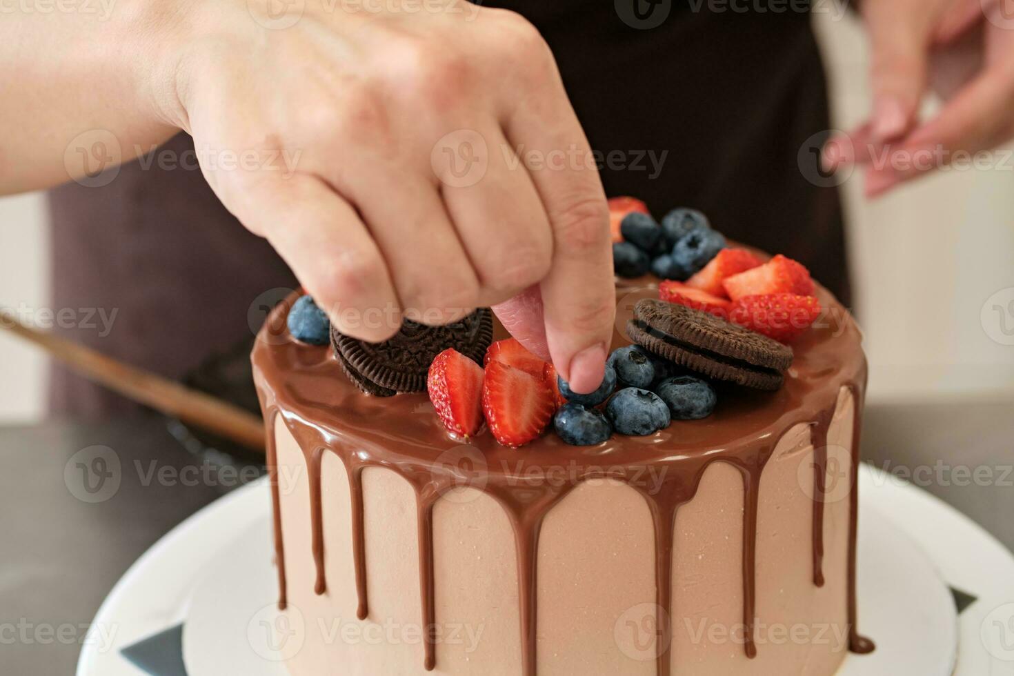 Woman pastry chef decorates chocolate cake with berries and cookies, close-up. Cake making process, Selective focus photo