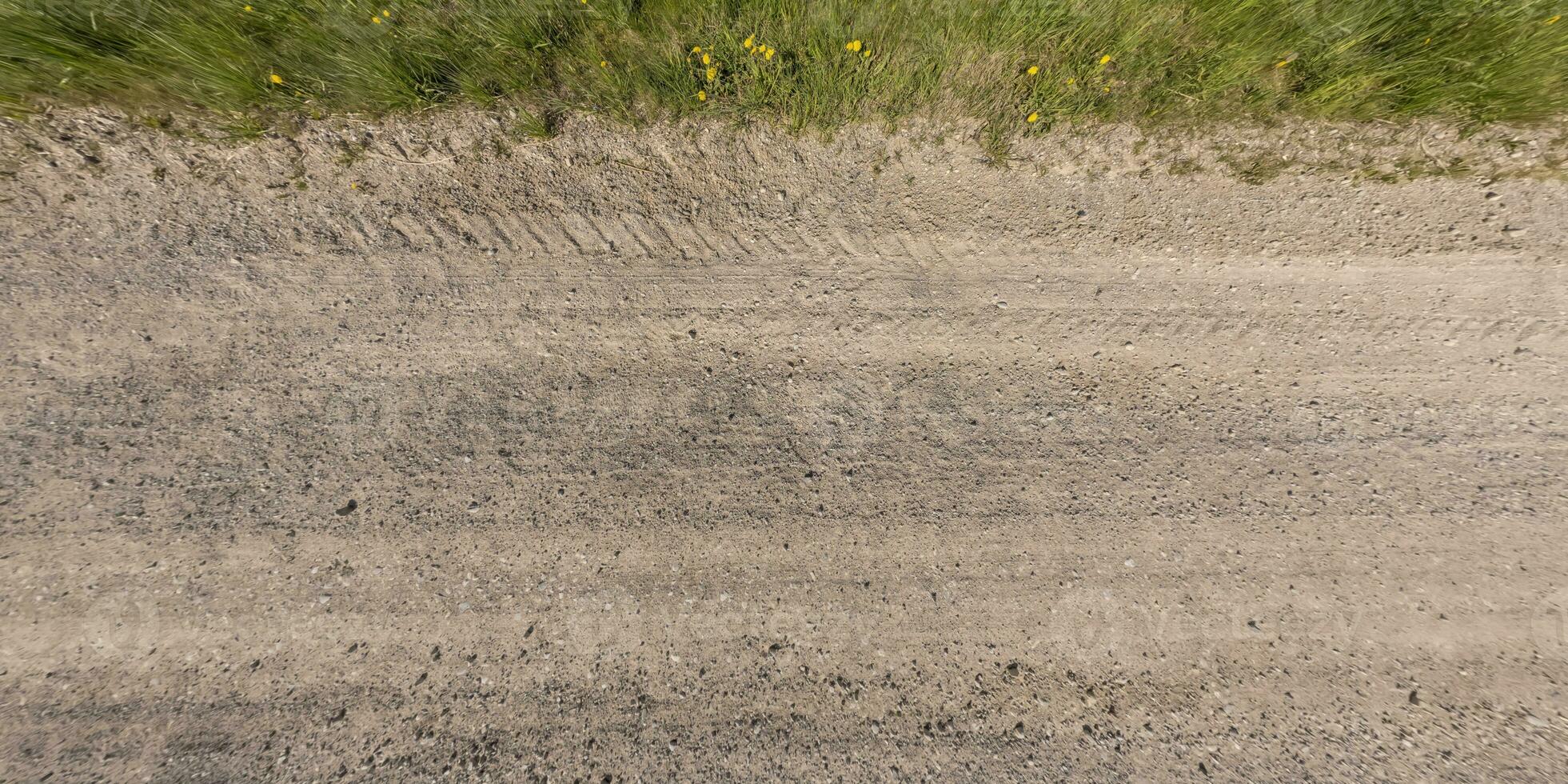 panorama of surface from above of gravel road with car tire tracks with roadside and grass photo