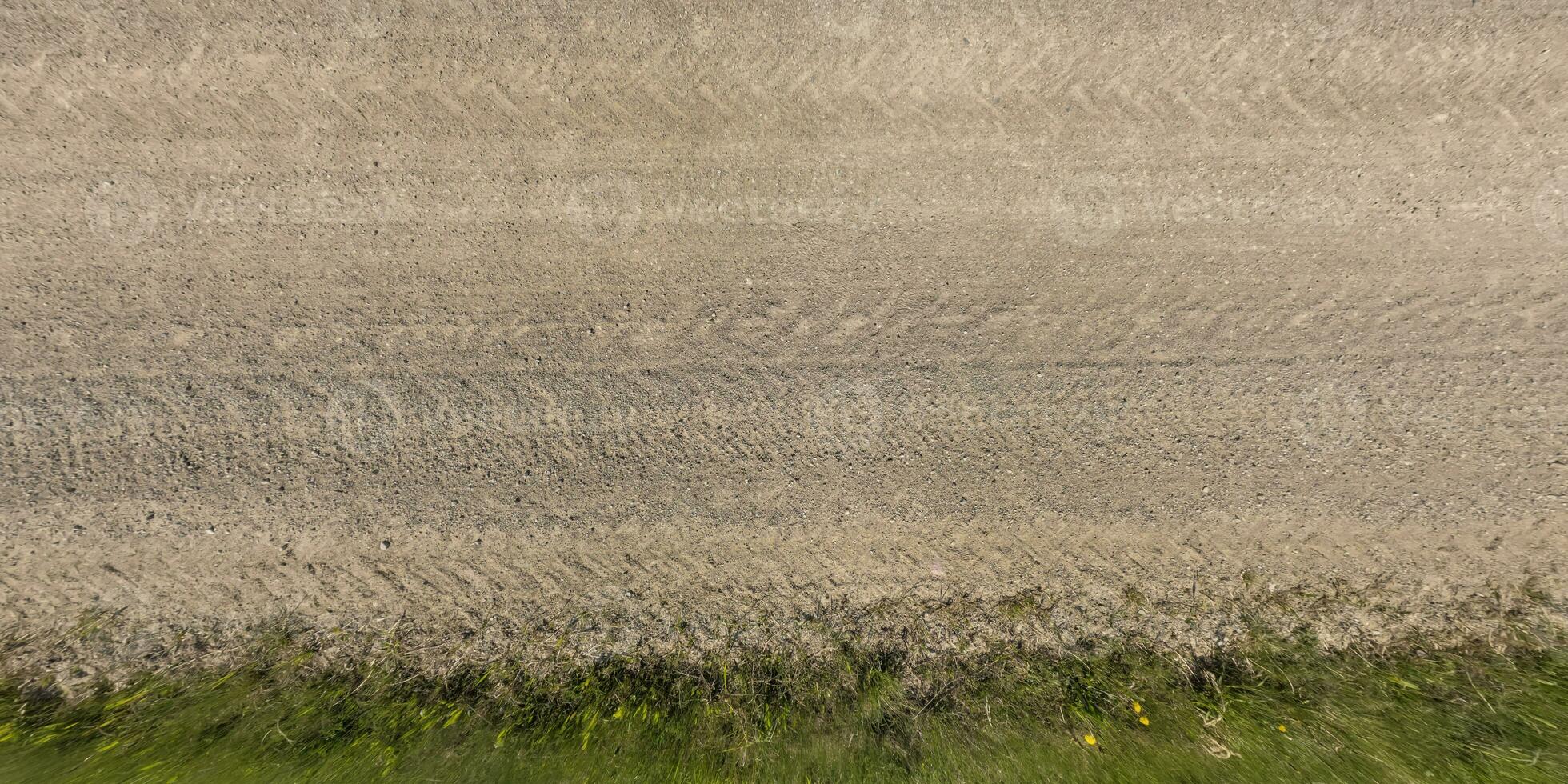 panorama of surface from above of gravel road with car tire tracks with roadside and grass photo