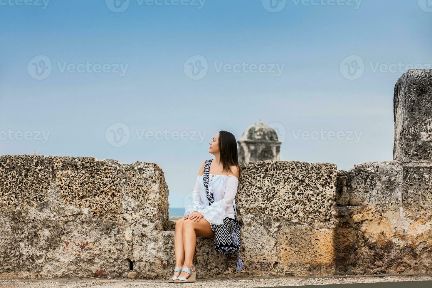 Beautiful woman on white dress sitting alone at the walls surrounding the colonial city of Cartagena de Indias photo