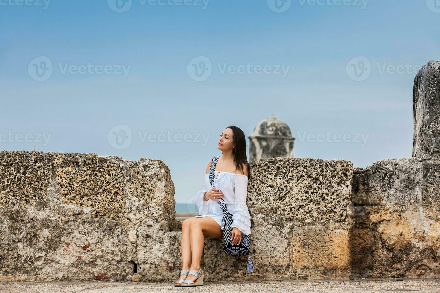 Beautiful woman on white dress sitting alone at the walls surrounding the colonial city of Cartagena de Indias photo