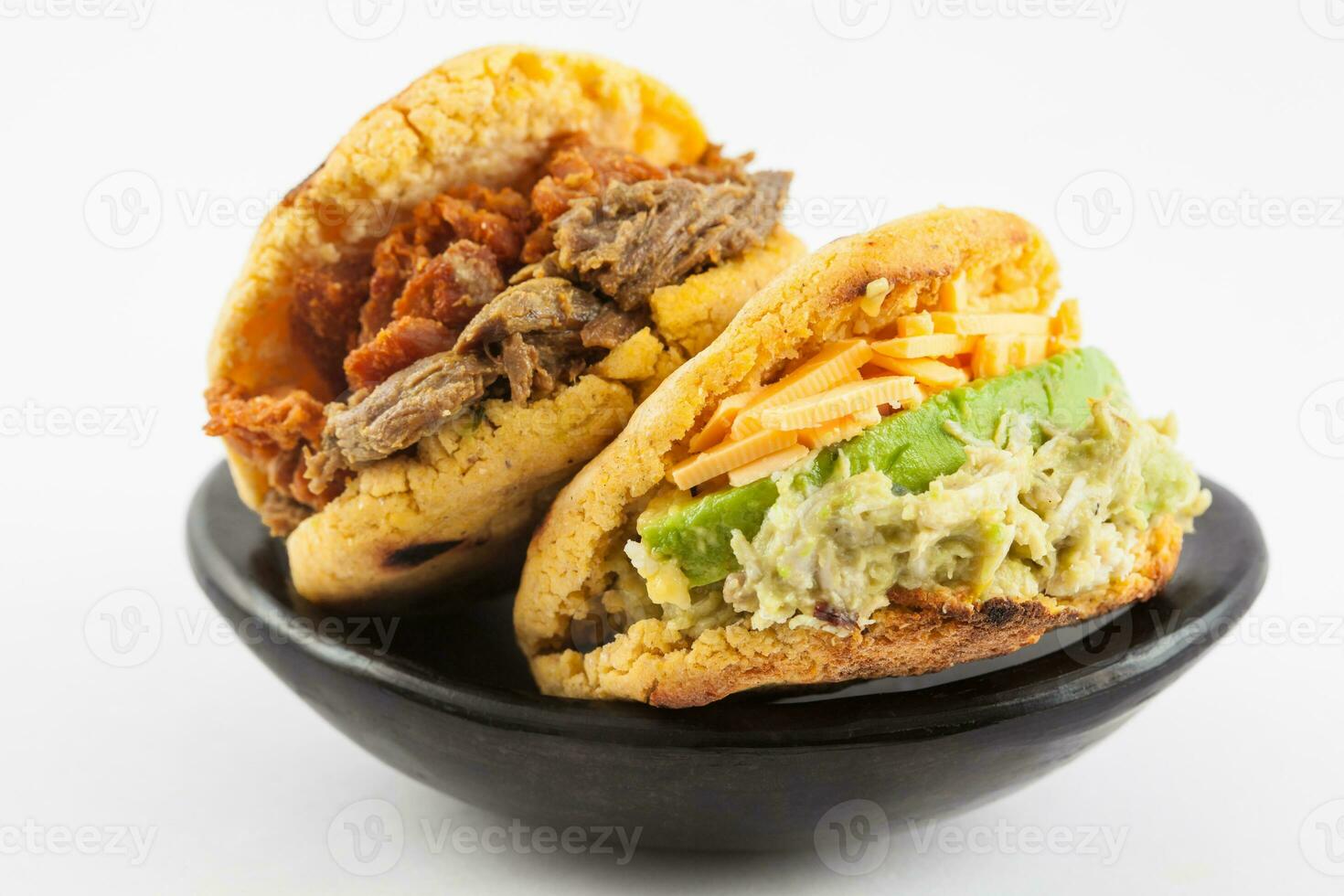 Arepas with two different fillings served in a black ceramic dish on white background photo